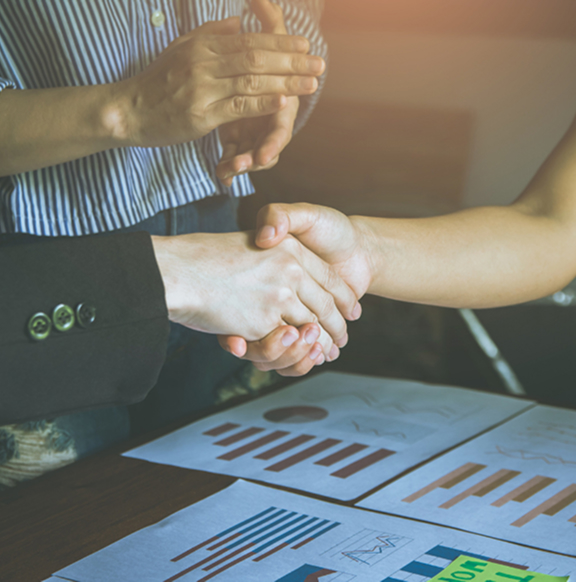 time de stakeholders celebra com um aperto de mão sobre uma mesa com planilhas e documentos. 
